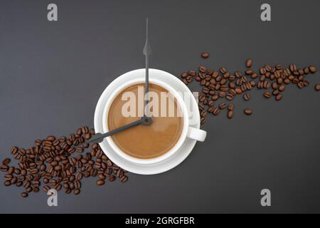 Coffee with milk and clock tongues showing 8 o`clock isolated on black. Stock Photo
